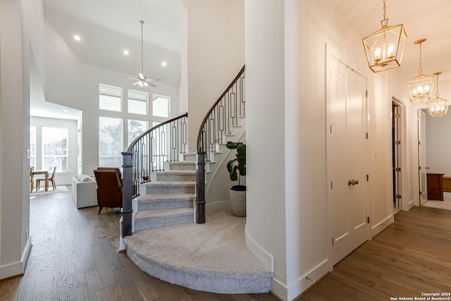 staircase with hardwood / wood-style flooring, ceiling fan with notable chandelier, and a high ceiling