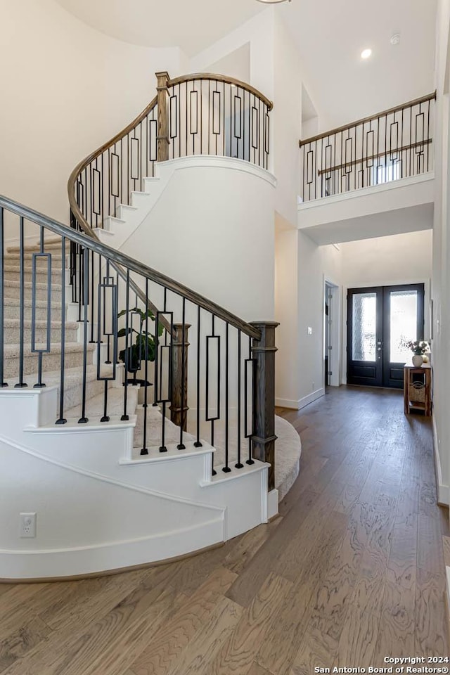 stairway with french doors, a high ceiling, and hardwood / wood-style floors