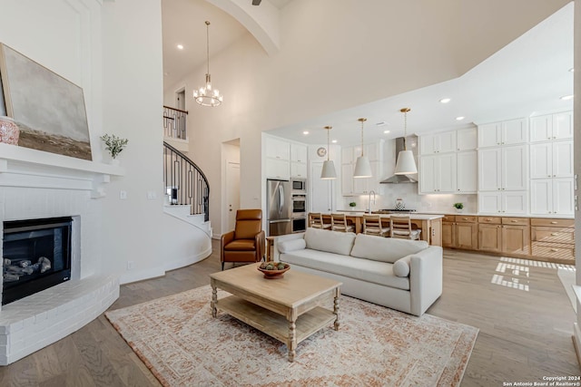 living room featuring beam ceiling, high vaulted ceiling, a notable chandelier, a fireplace, and light wood-type flooring