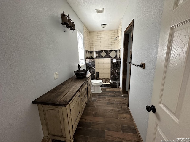 bathroom featuring vanity, a tile shower, a textured ceiling, and toilet