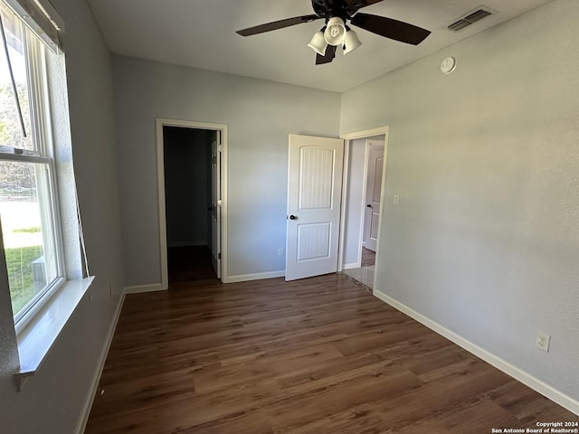 empty room with a wealth of natural light, ceiling fan, and dark wood-type flooring