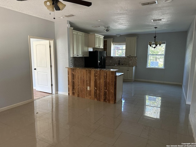 kitchen with tasteful backsplash, black fridge, decorative light fixtures, cream cabinetry, and light tile patterned floors