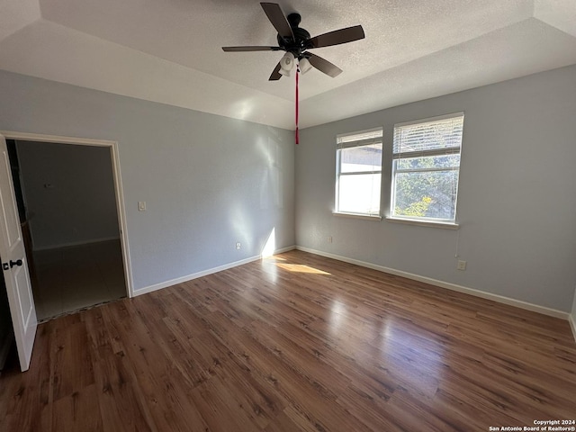 empty room with ceiling fan, dark hardwood / wood-style flooring, lofted ceiling, a textured ceiling, and a tray ceiling