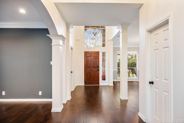 entryway with dark wood-type flooring, an inviting chandelier, ornamental molding, and ornate columns