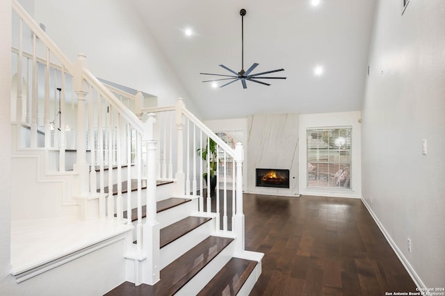 staircase featuring ceiling fan, hardwood / wood-style floors, a high end fireplace, and high vaulted ceiling