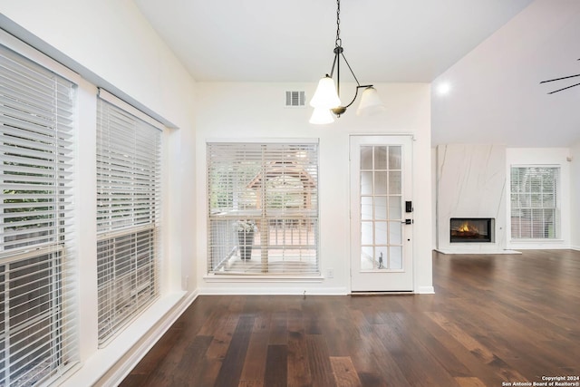 unfurnished dining area with ceiling fan with notable chandelier, dark wood-type flooring, and a premium fireplace