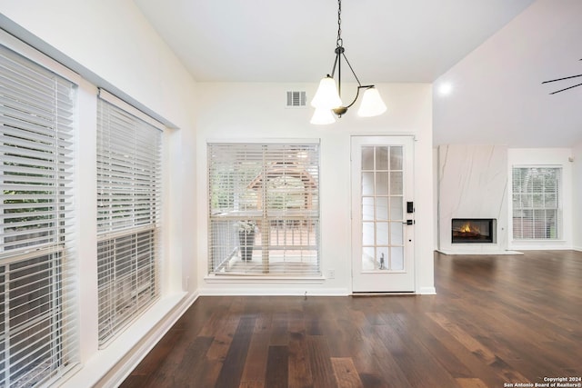 unfurnished dining area with ceiling fan with notable chandelier, a healthy amount of sunlight, dark hardwood / wood-style flooring, and a fireplace