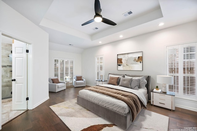 bedroom with ceiling fan, dark hardwood / wood-style flooring, a tray ceiling, and ensuite bath