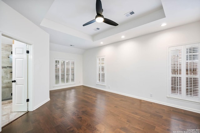 spare room featuring a raised ceiling, ceiling fan, and dark wood-type flooring