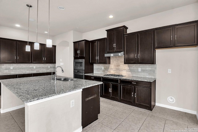 kitchen with hanging light fixtures, sink, light stone countertops, an island with sink, and appliances with stainless steel finishes