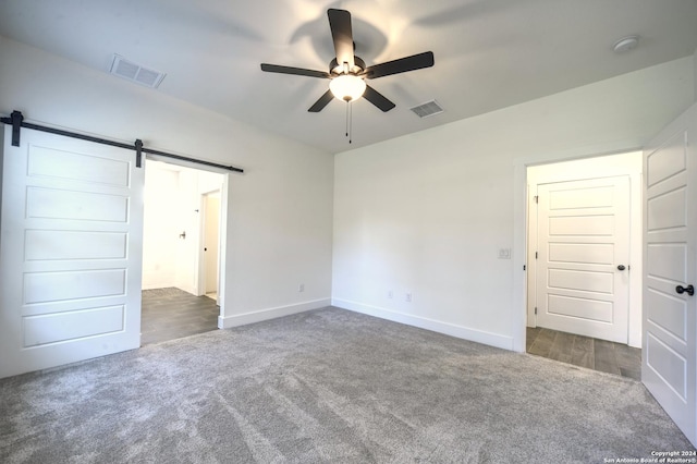 unfurnished bedroom featuring ceiling fan, a barn door, and dark carpet