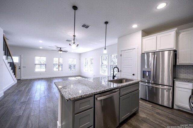 kitchen with ceiling fan, sink, stainless steel appliances, dark hardwood / wood-style floors, and a center island with sink