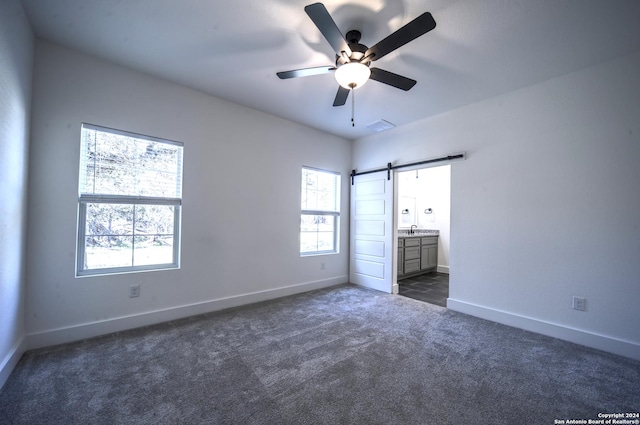 unfurnished bedroom featuring multiple windows, a barn door, ensuite bathroom, and ceiling fan