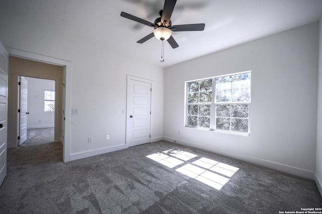 unfurnished bedroom with multiple windows, ceiling fan, and dark colored carpet