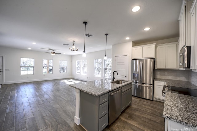 kitchen with appliances with stainless steel finishes, ceiling fan with notable chandelier, sink, white cabinets, and an island with sink