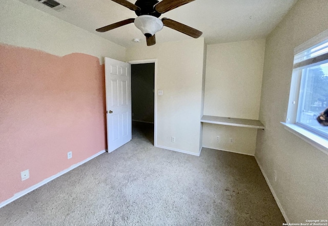 unfurnished bedroom featuring multiple windows, built in desk, light colored carpet, and ceiling fan