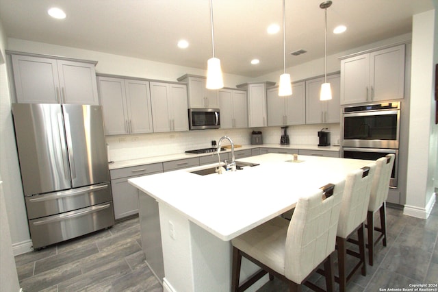 kitchen with appliances with stainless steel finishes, sink, pendant lighting, a center island with sink, and a breakfast bar area