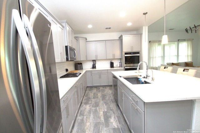 kitchen featuring gray cabinetry, sink, decorative backsplash, an island with sink, and appliances with stainless steel finishes