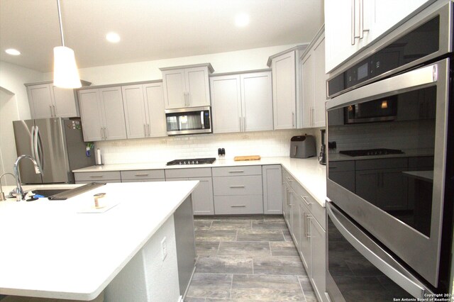 kitchen featuring gray cabinetry, sink, decorative light fixtures, decorative backsplash, and appliances with stainless steel finishes