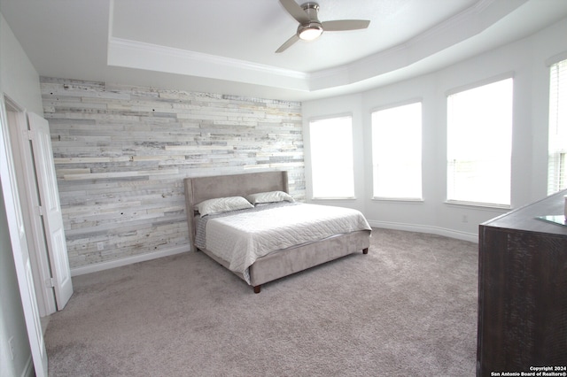 carpeted bedroom with a tray ceiling, wood walls, and ceiling fan