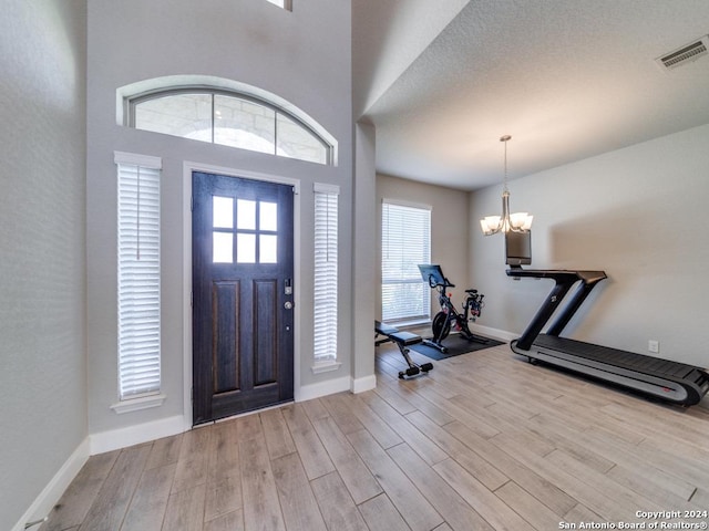 foyer entrance with a wealth of natural light, light hardwood / wood-style floors, a textured ceiling, and an inviting chandelier