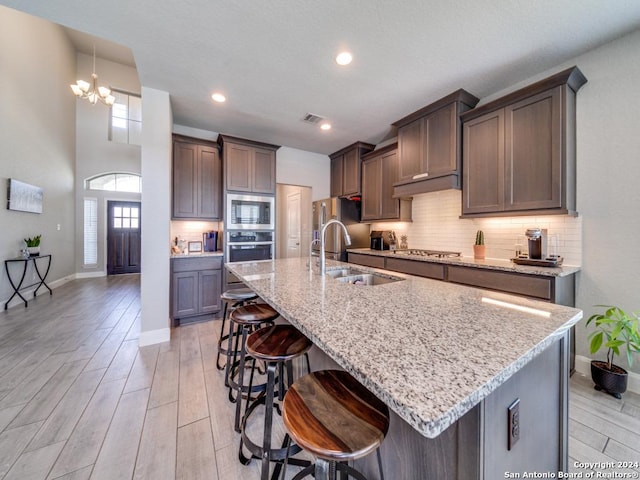 kitchen featuring stainless steel appliances, a kitchen island with sink, a notable chandelier, and sink