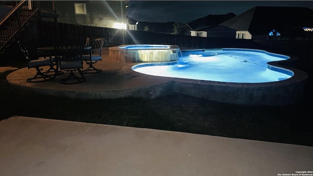 pool at twilight featuring pool water feature, a patio area, and an in ground hot tub