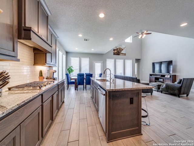 kitchen with light stone countertops, ceiling fan, sink, a textured ceiling, and a center island with sink