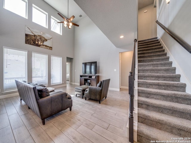 living room featuring a towering ceiling, ceiling fan, and a healthy amount of sunlight