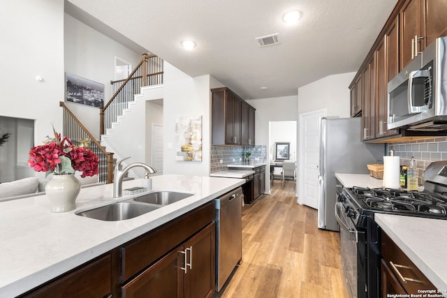 kitchen with appliances with stainless steel finishes, tasteful backsplash, dark brown cabinetry, sink, and light hardwood / wood-style flooring