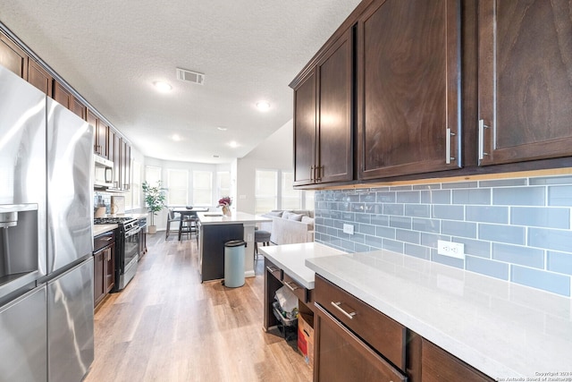 kitchen featuring decorative backsplash, dark brown cabinets, a textured ceiling, stainless steel appliances, and light hardwood / wood-style floors