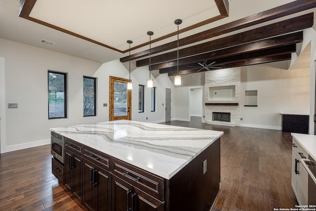 kitchen with dark hardwood / wood-style flooring, decorative light fixtures, a center island, a stone fireplace, and stainless steel microwave