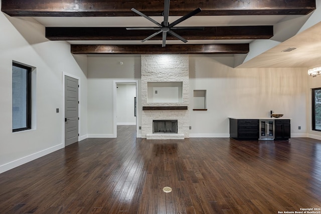 unfurnished living room with dark hardwood / wood-style flooring, a fireplace, beamed ceiling, and ceiling fan with notable chandelier