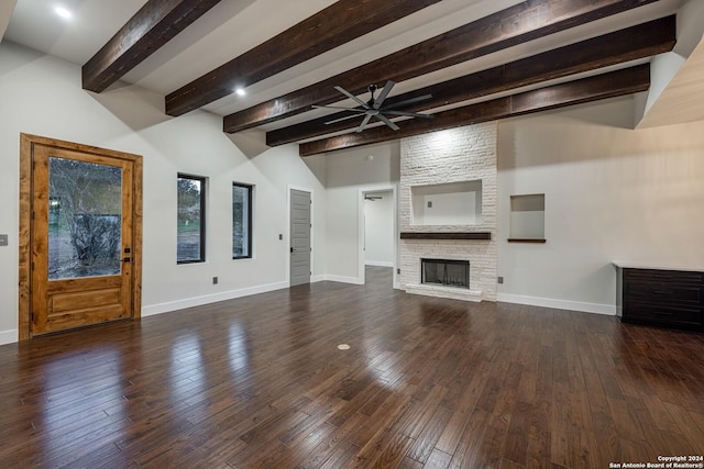 unfurnished living room featuring ceiling fan, beam ceiling, a stone fireplace, and dark wood-type flooring