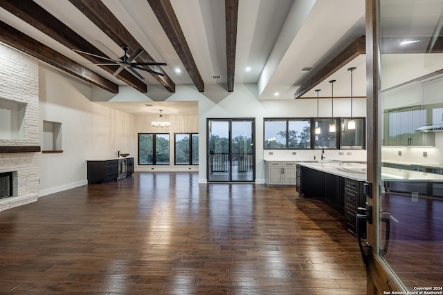 interior space with sink, dark wood-type flooring, beamed ceiling, a fireplace, and ceiling fan with notable chandelier