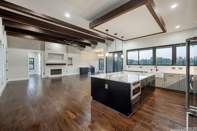 kitchen with a center island, ceiling fan with notable chandelier, light stone countertops, a fireplace, and beamed ceiling