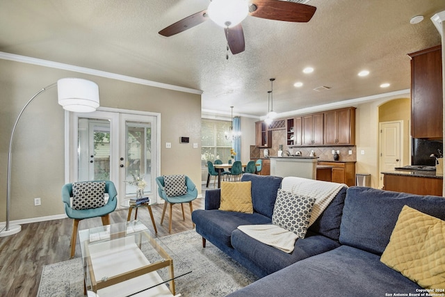 living room featuring a textured ceiling, light wood-type flooring, crown molding, and french doors