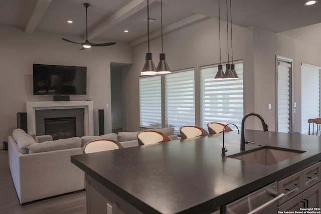 kitchen with ceiling fan, sink, beamed ceiling, hanging light fixtures, and a tiled fireplace