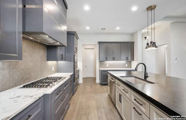 kitchen with sink, wall chimney exhaust hood, light wood-type flooring, decorative light fixtures, and stainless steel appliances