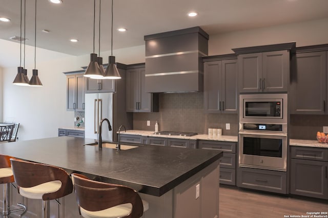 kitchen with hanging light fixtures, sink, stainless steel appliances, and a kitchen island with sink