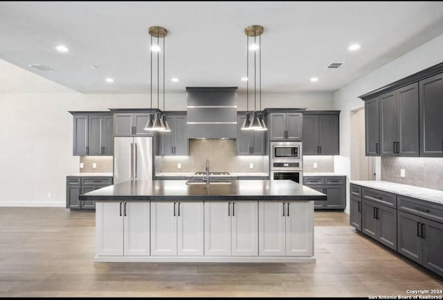 kitchen with a kitchen island with sink, pendant lighting, and appliances with stainless steel finishes