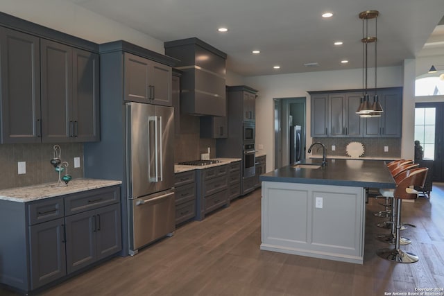 kitchen with sink, hanging light fixtures, stainless steel appliances, dark hardwood / wood-style floors, and a center island with sink