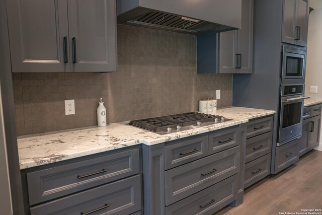 kitchen featuring decorative backsplash, stainless steel appliances, wall chimney range hood, wood-type flooring, and gray cabinets