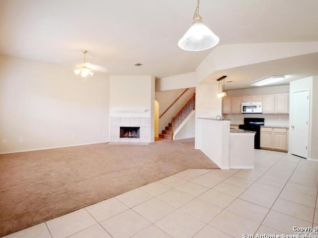 kitchen with light carpet, vaulted ceiling, pendant lighting, black range, and a tiled fireplace