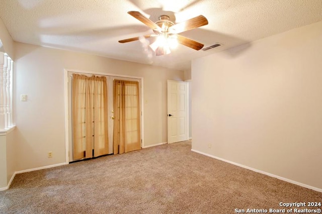 unfurnished bedroom with ceiling fan, light colored carpet, and a textured ceiling