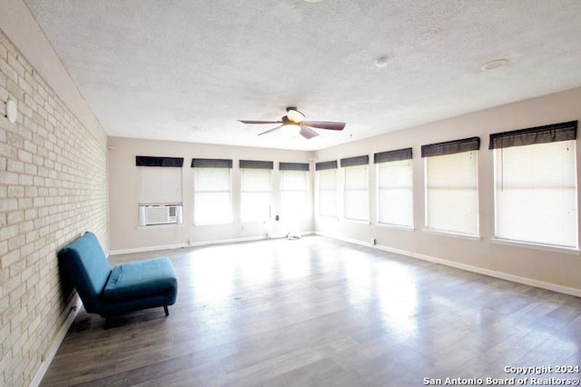 unfurnished room with ceiling fan, brick wall, hardwood / wood-style floors, cooling unit, and a textured ceiling