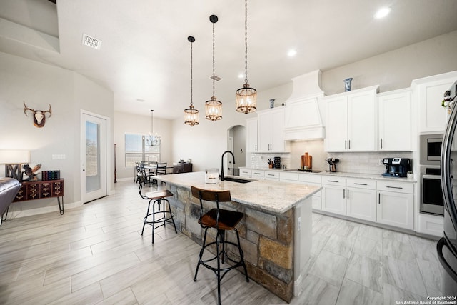 kitchen featuring a kitchen breakfast bar, sink, white cabinets, hanging light fixtures, and an island with sink