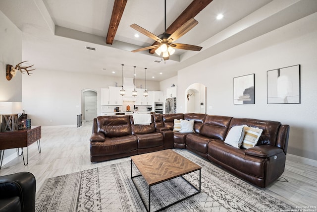 living room with beam ceiling, ceiling fan, a high ceiling, a tray ceiling, and light wood-type flooring