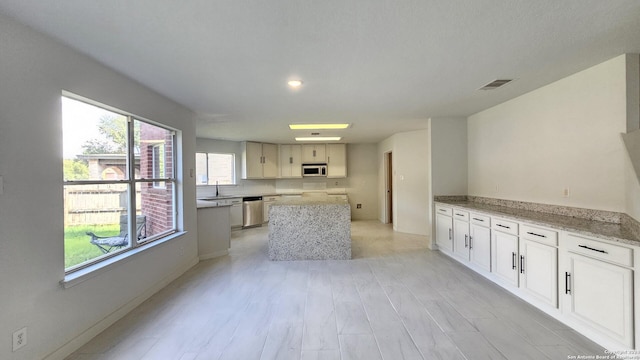 kitchen featuring white cabinetry, dishwasher, and light stone countertops