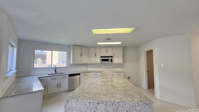 kitchen featuring light stone counters, a textured ceiling, sink, dishwasher, and a center island